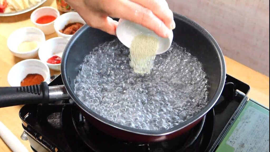 沸騰した水に鶏ガラスープの素を入れている画像