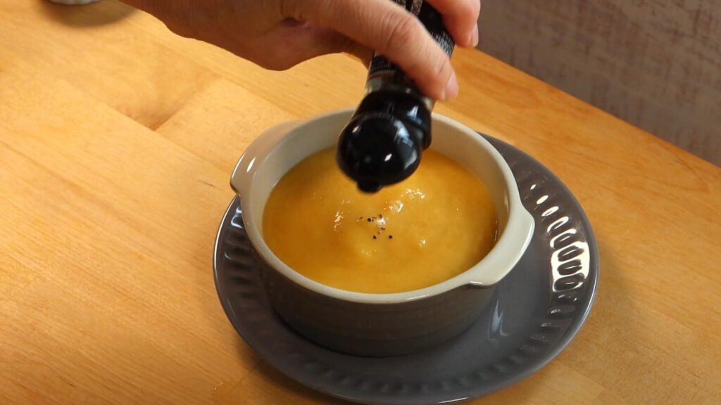 器に盛ったスープにブラックペッパーを加えている画像