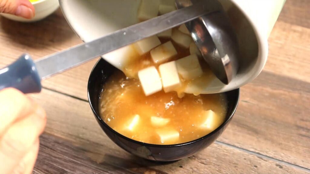 豆腐の味噌スープを器に盛っている画像